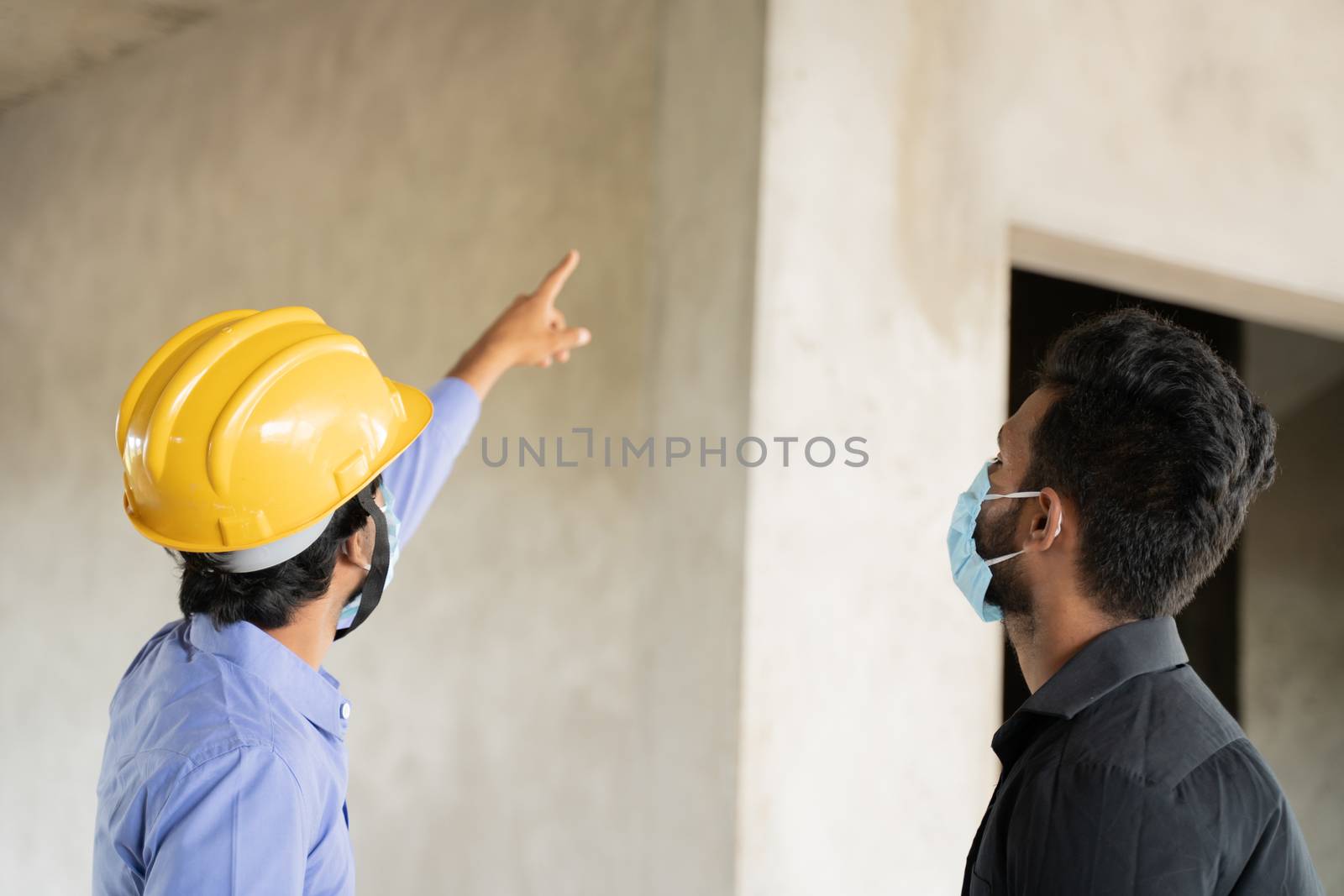 Two construction worker in medical mask busy in work while maintaining social distancing - concept of covid-19 or coronavirus safety measures at work place