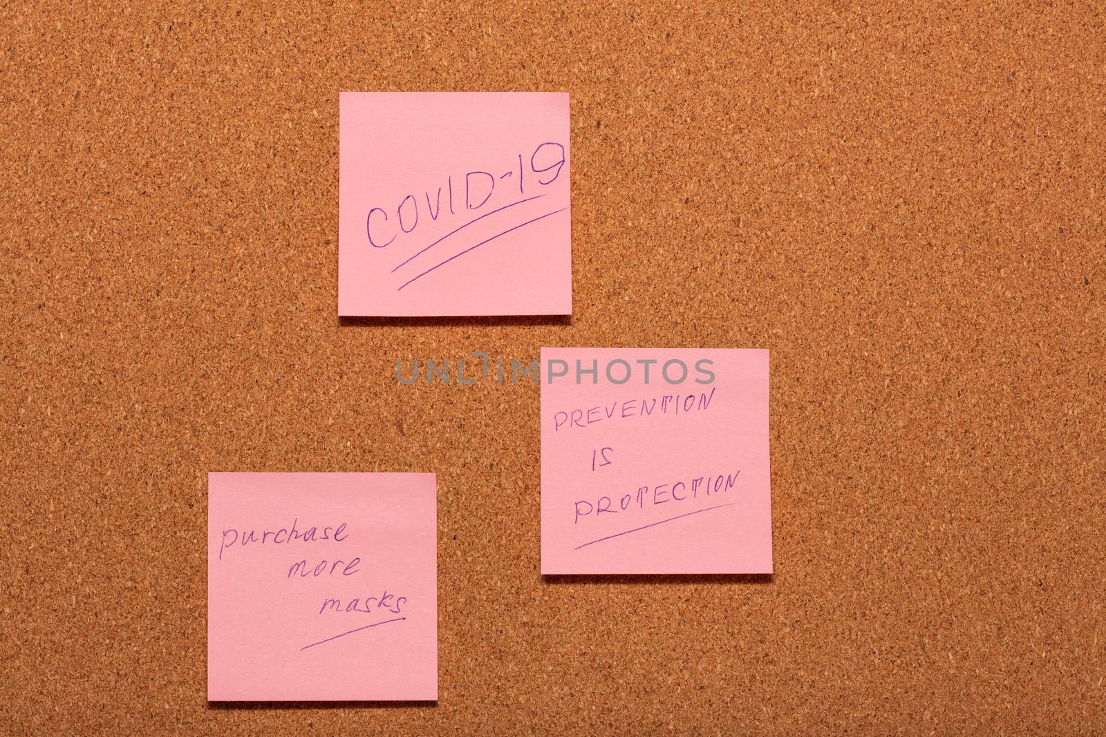Covid-19, Prevention is Protection, and reminder to purchase more masks handwritten on three pink stickers on a cork notice-board. Healthcare and social concepts.
