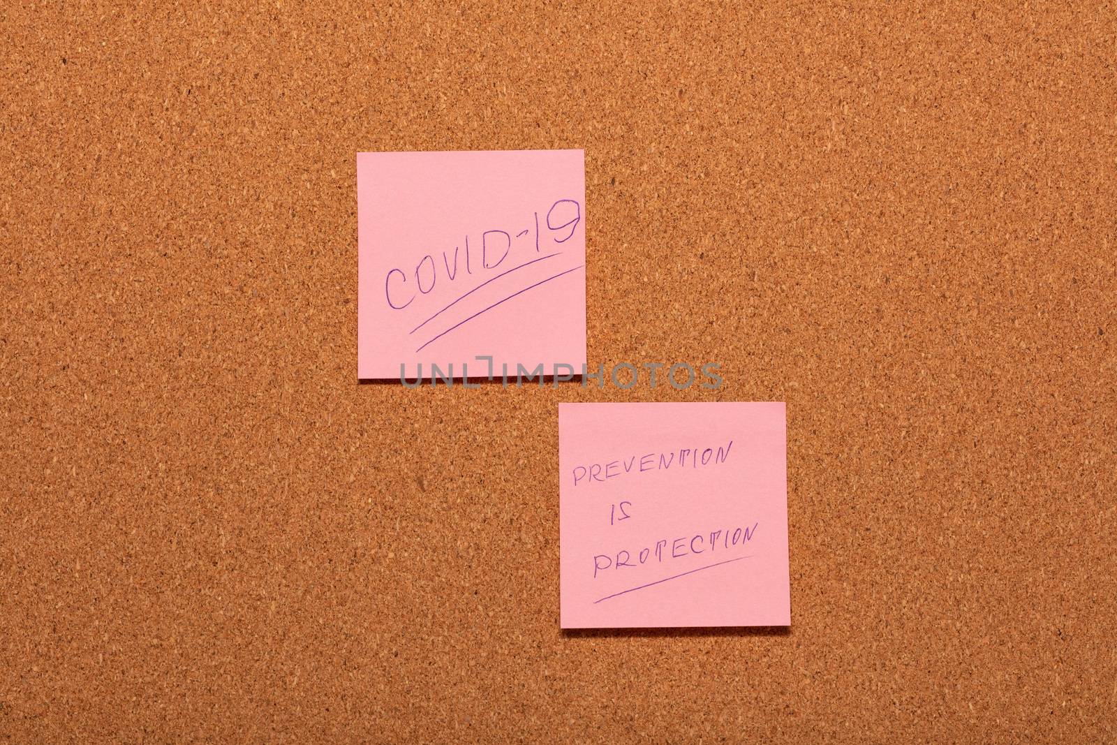 Covid-19 and Prevention is Protection handwritten on two pink stickers on a cork notice-board. by DamantisZ