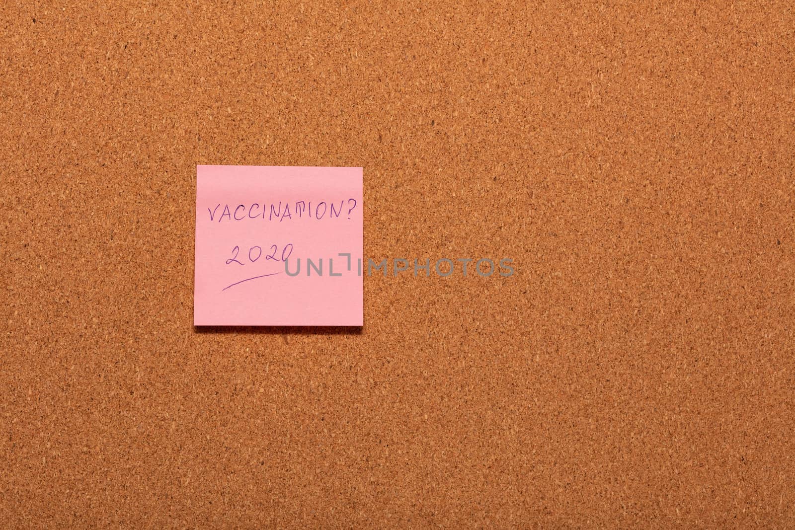 Vaccination 2020? handwritten on a pink sticker on a cork notice-board. by DamantisZ