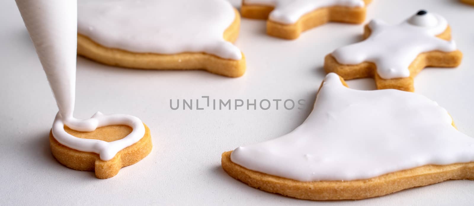 Close up of decorating cute Halloween gingerbread cookies with frosting icing cream topping bag.