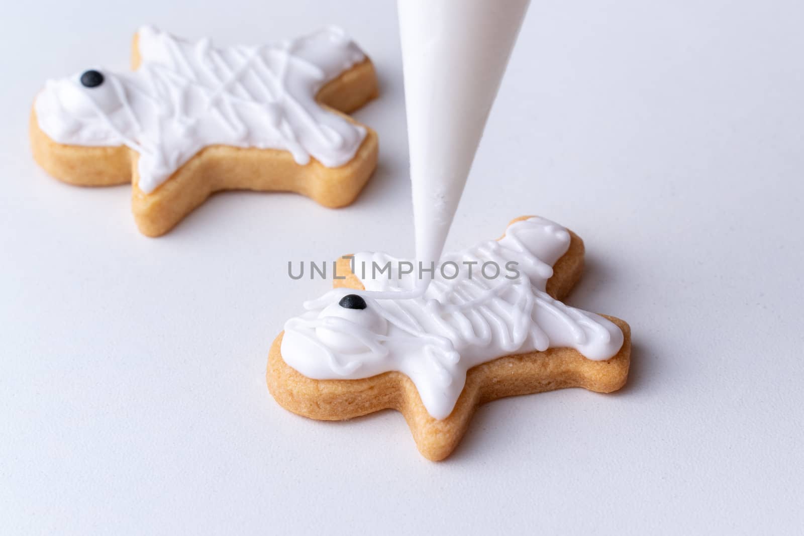 Close up of decorating cute Halloween gingerbread cookies with frosting icing cream topping bag.