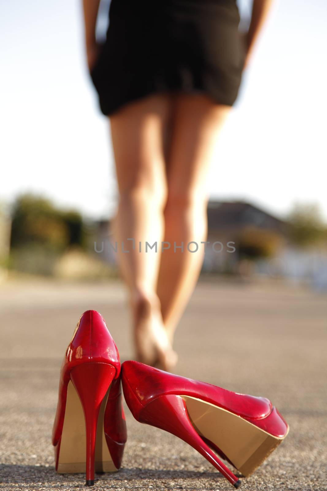 Red high heels standing on the street an a woman goes away barefoot