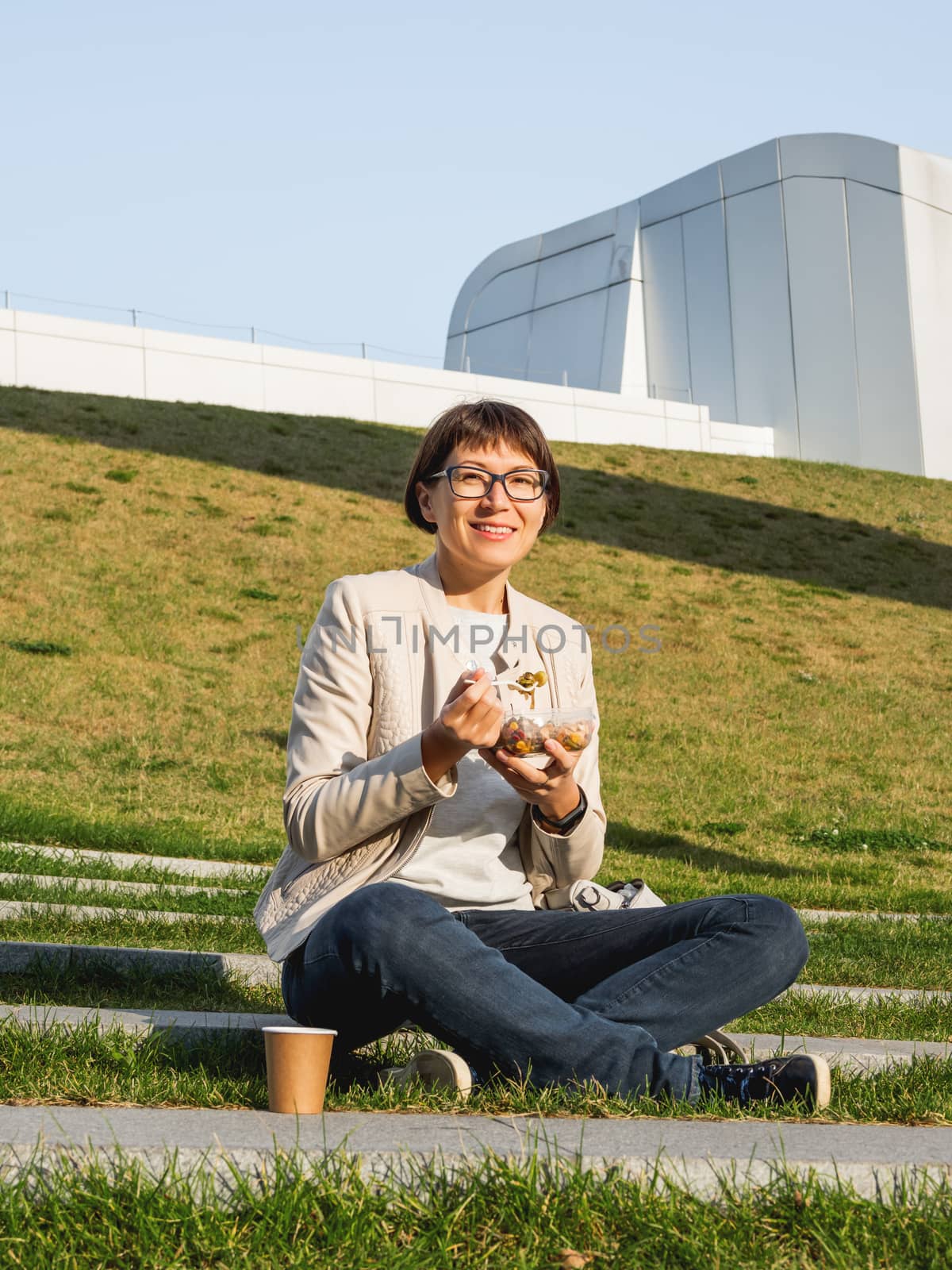 Woman sits on park bench with take away lunch box, cardboard cup by aksenovko