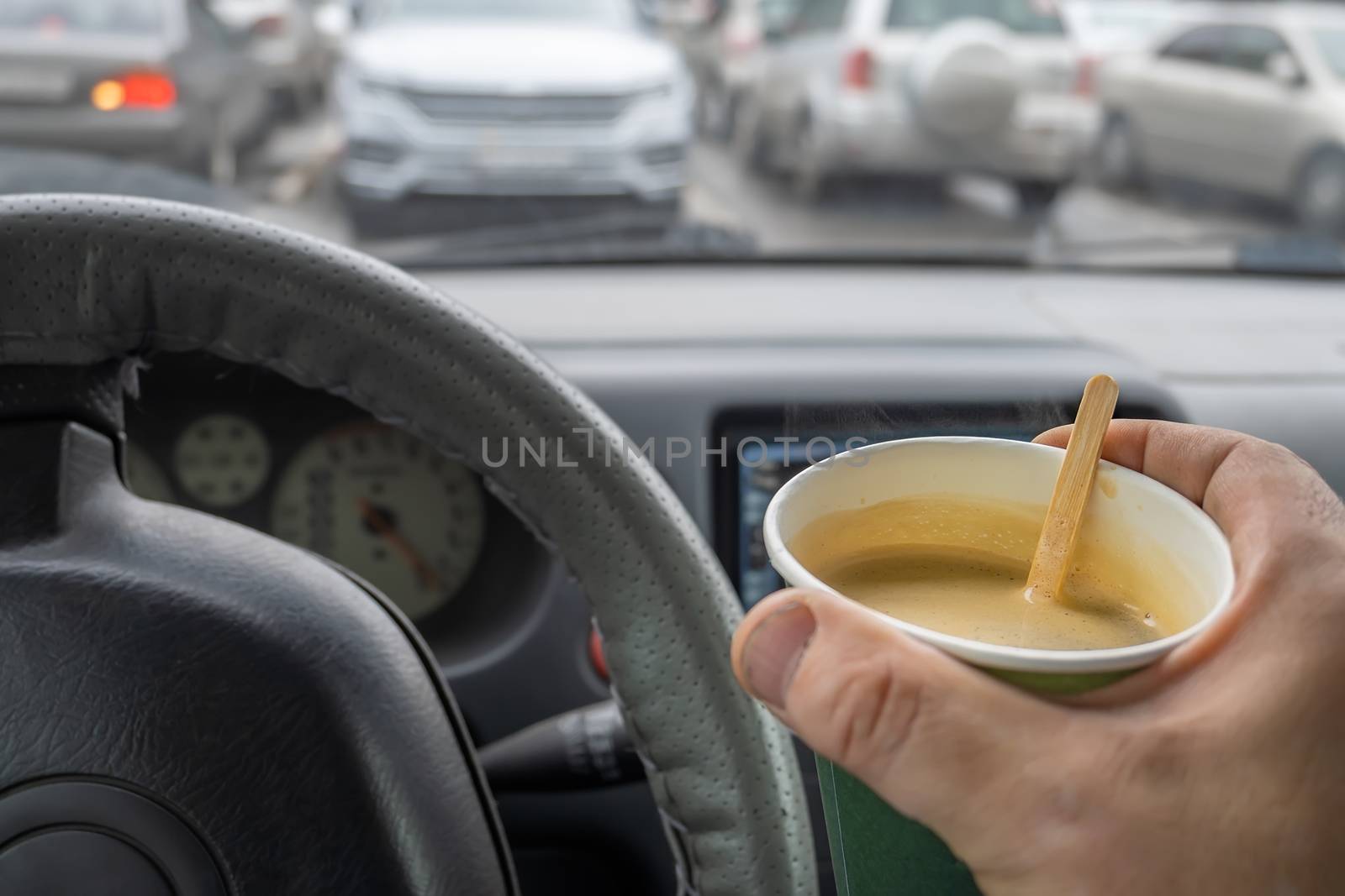 hand of the car driver who is sitting in the car, holding a Cup of coffee, cocoa in the Parking lot