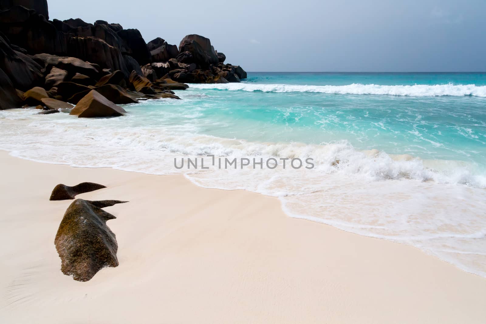 Blue sky and a white sand beach with a lot of big rocks