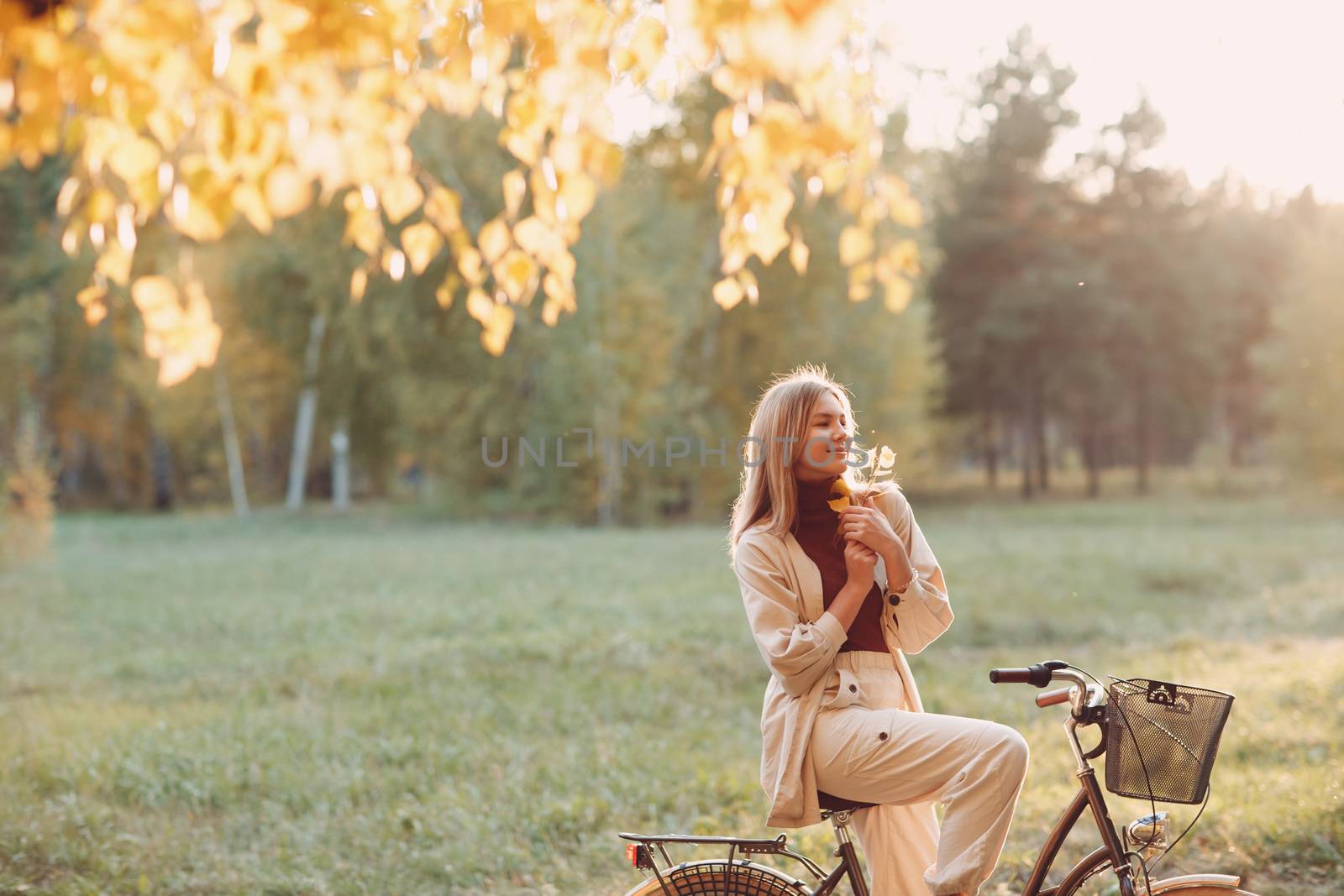 Happy active young woman holds fall leaves in hand ride bicycle in autumn park by primipil