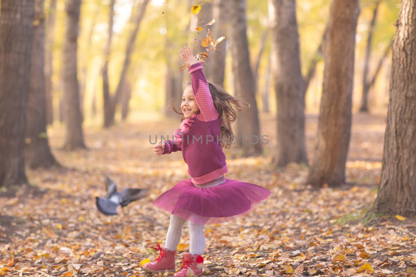 Cute little girl in autumn park with orange and yellow color leaves and flying bird by primipil
