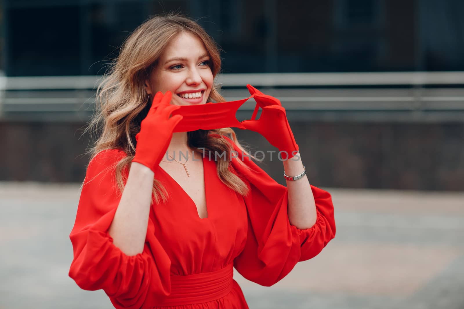 Young woman in red dress and gloves puts on medical face mask.