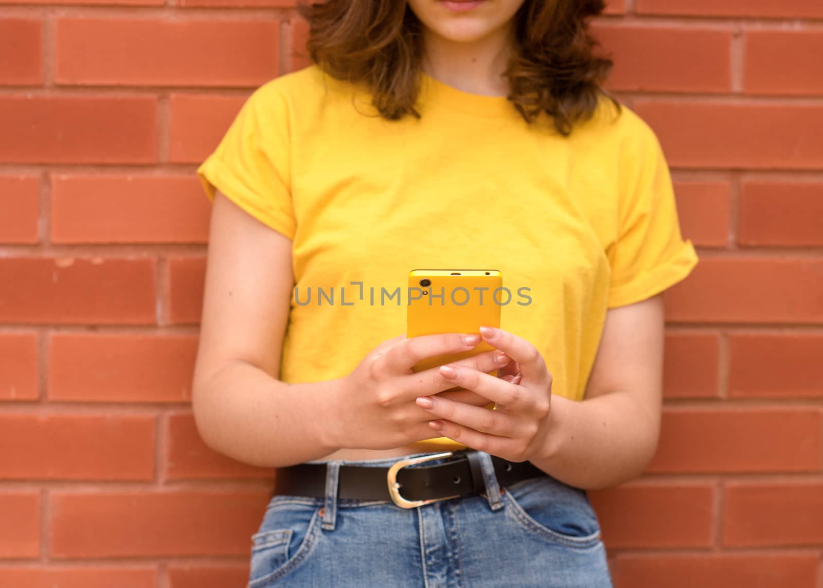 young woman wearing a yellow shirt, chatting on phone against a brick wall