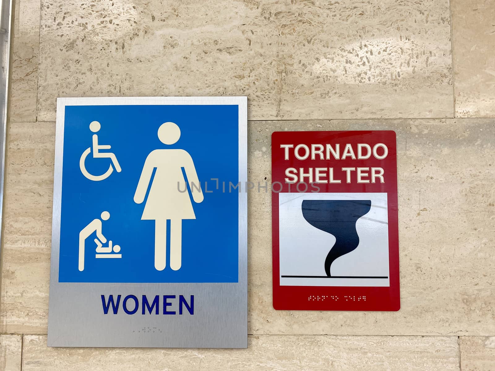 The women's restroom and tornado shelter signs directing people to the shelter in a public building.