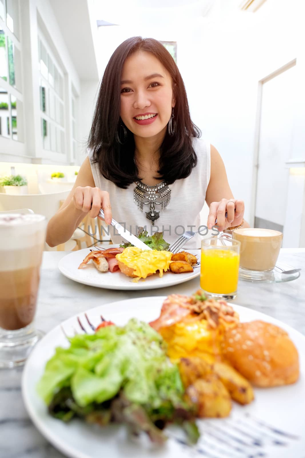 Young woman eating Breakfast - fried egg, beans, tomatoes, mushrooms, bacon and toast.