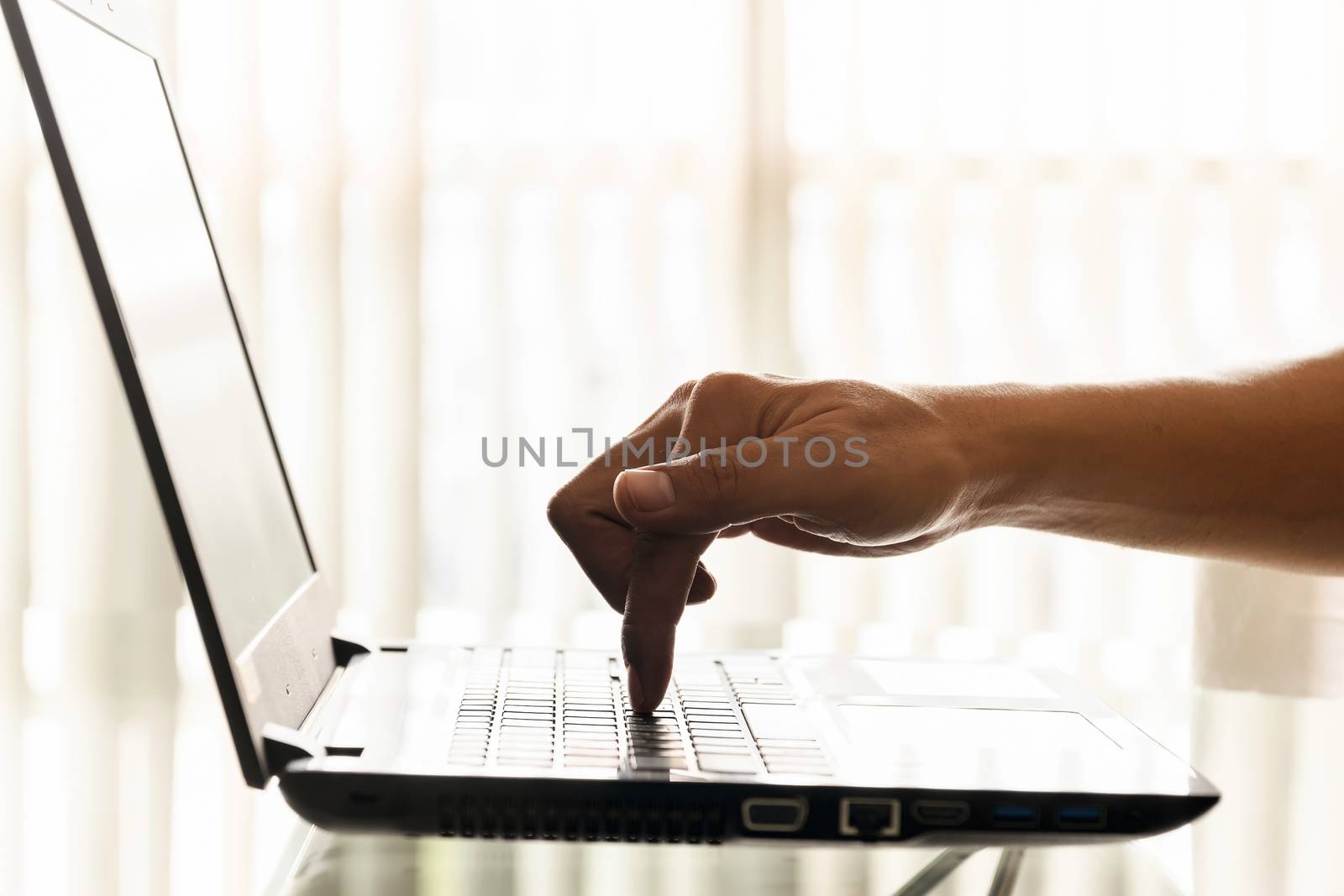 A businessman's finger is pressing down on the laptop's keyboard button in the office.