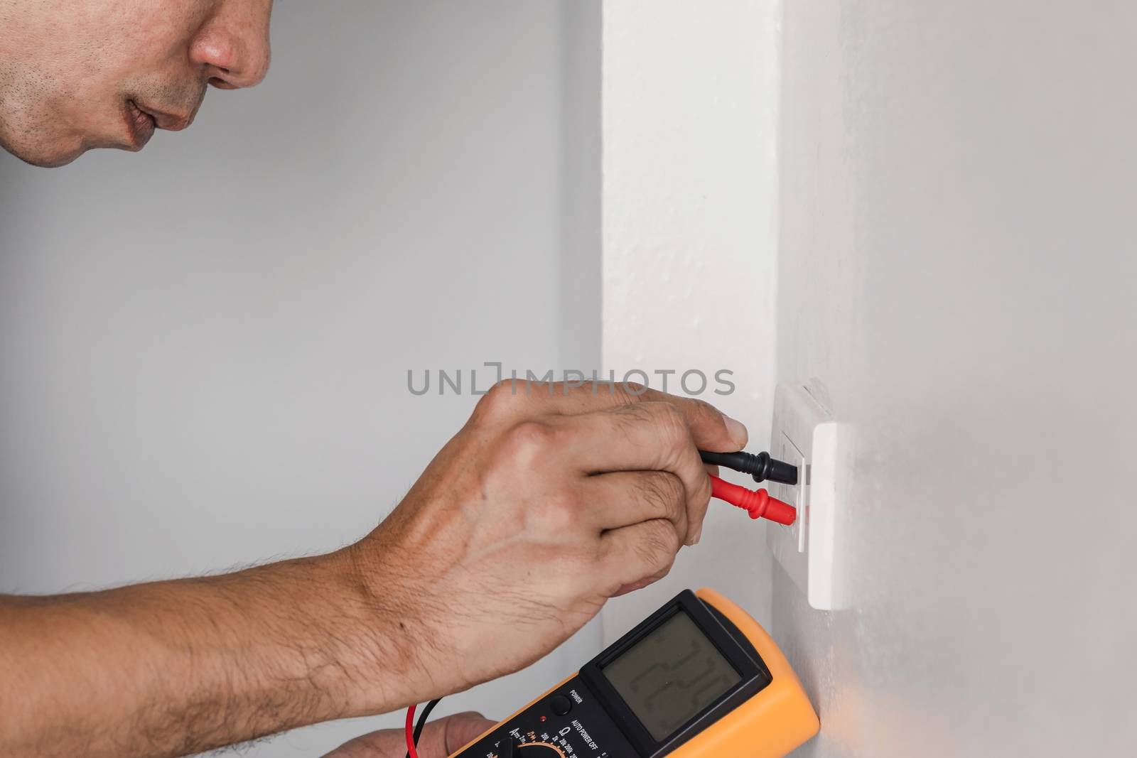 Electrician is using a digital meter to measure the voltage at the power outlet in on the wall.