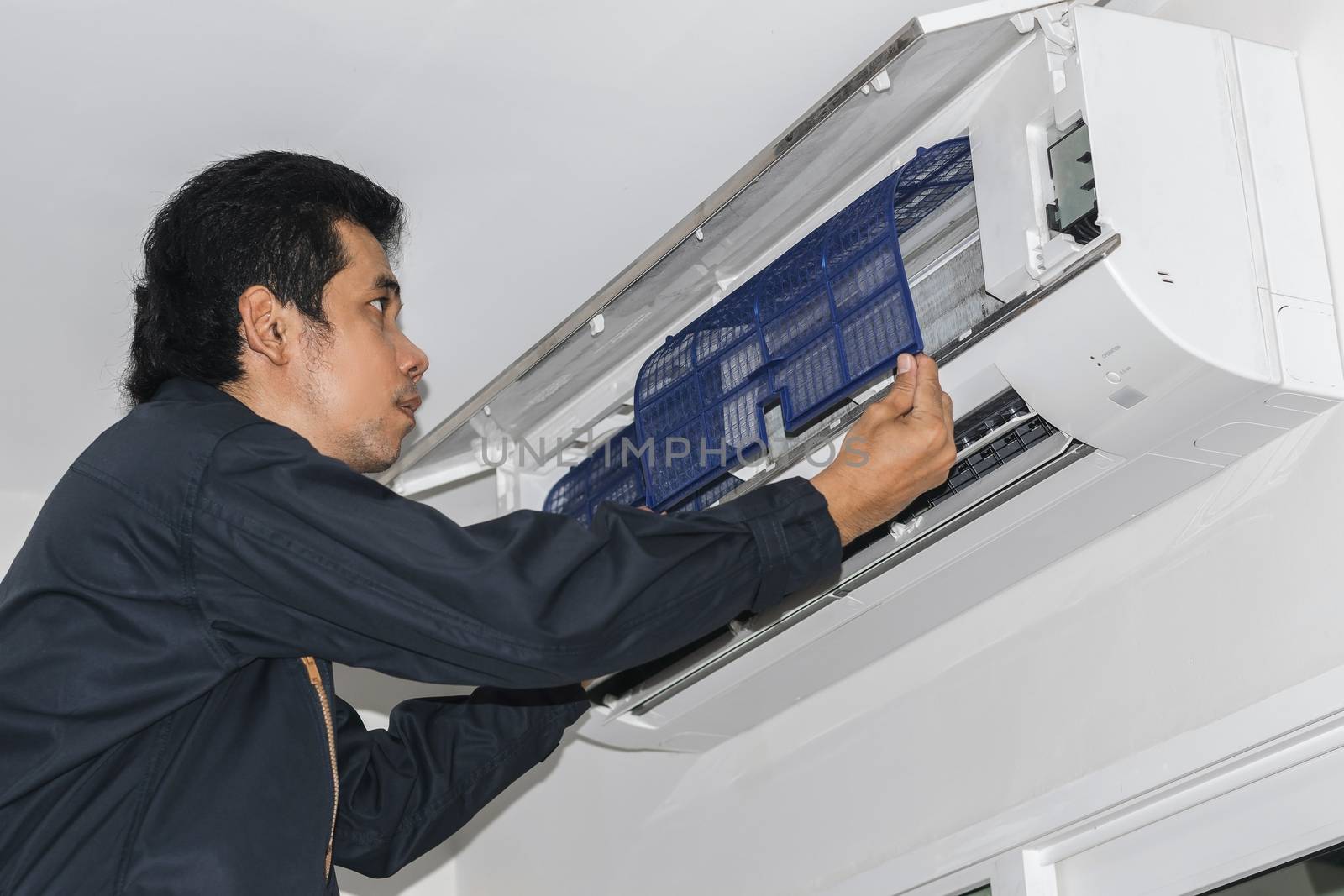 Air conditioner repairers in blue uniform are checking and repair air hanging on the wall.