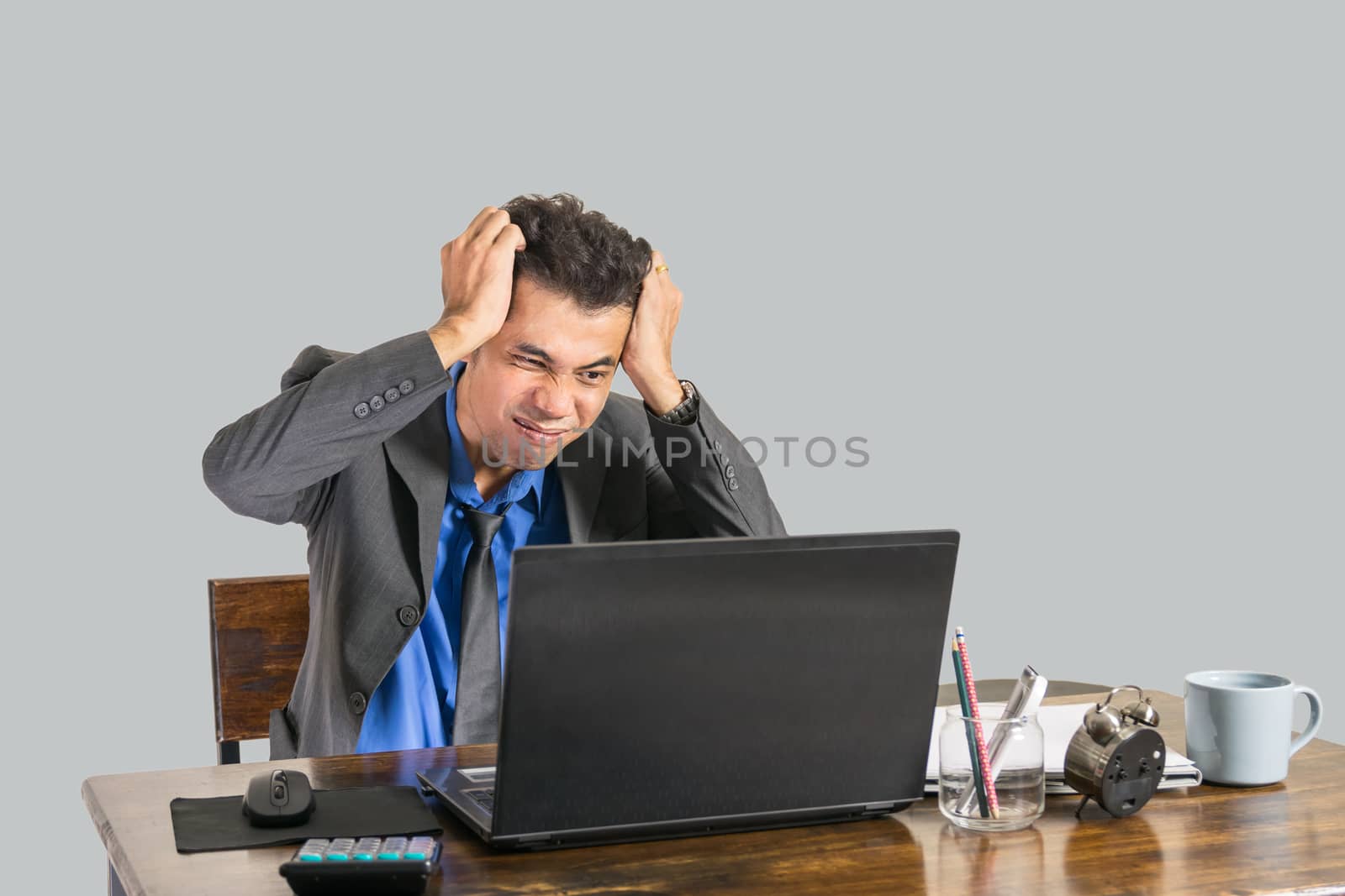 A young businessman wearing a suit was shocked when he looked at a laptop on a desk in his office, business people concept.