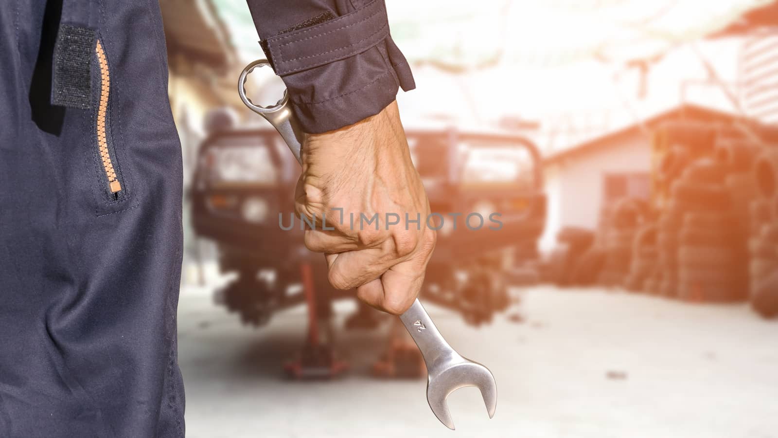 Car repairman wearing a dark blue uniform standing and holding a wrench that is an essential tool for a mechanic and has a backdrop as a car repair center, Automotive industry and garage concepts.