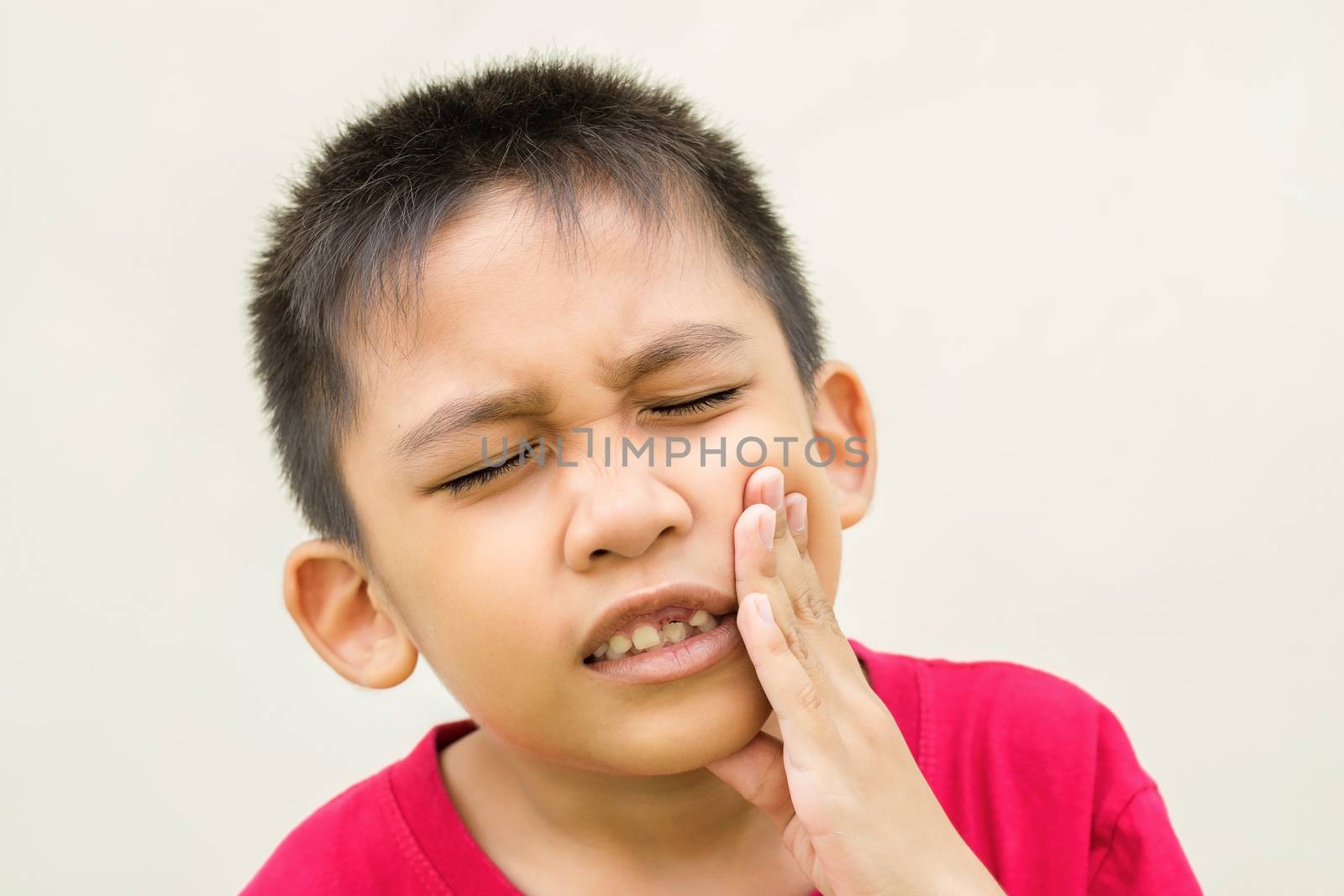 The boy is holding his hand on his cheek and red face with pain from toothache.