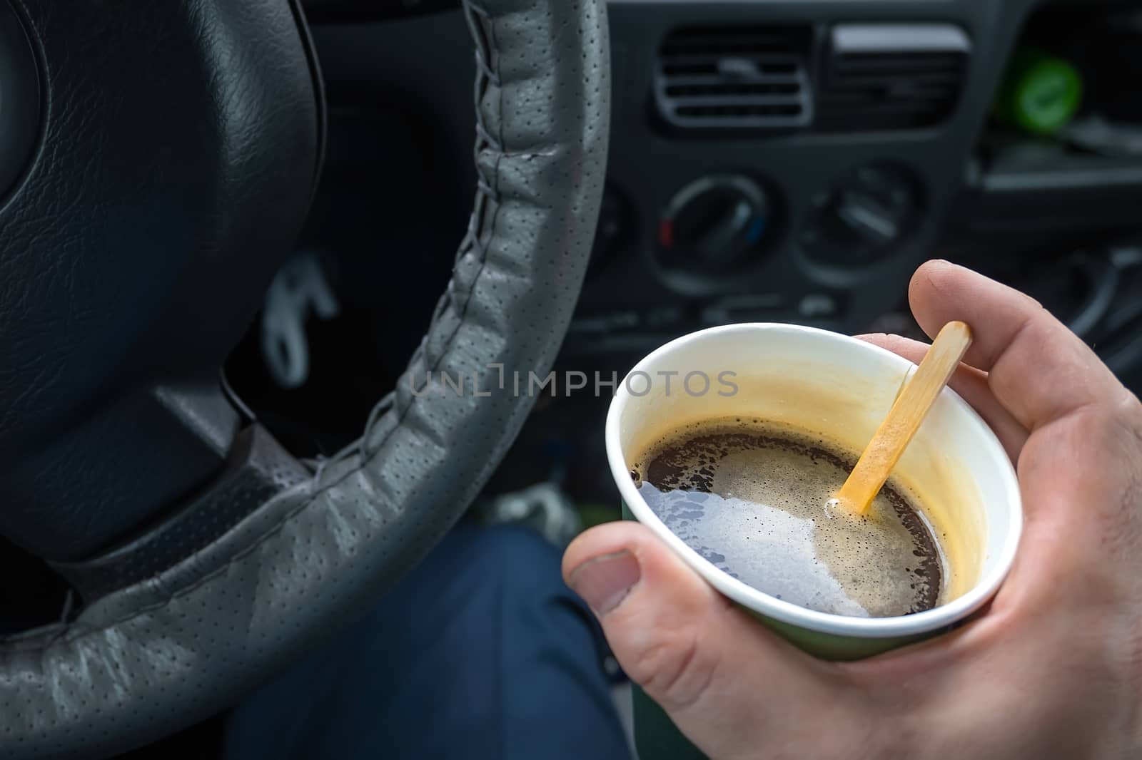 paper Cup of coffee in the driver hand at the wheel of the car closeup