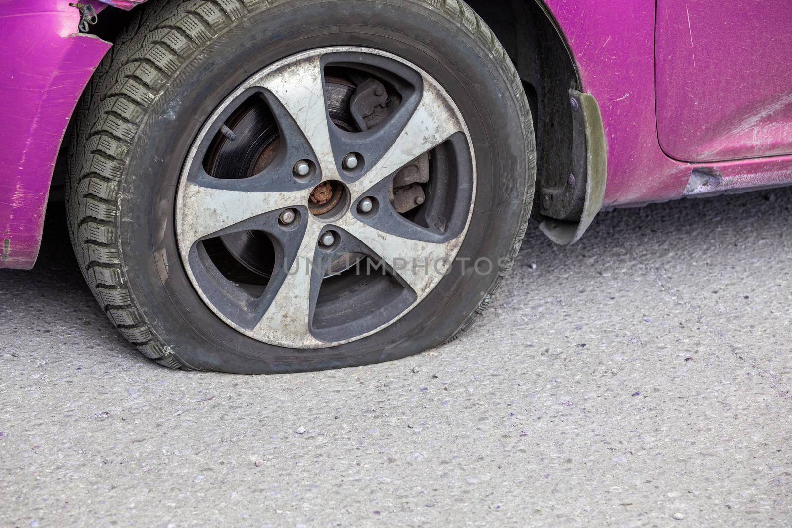 civil car flat tire close-up at dry sunny day on gray asphalt surface.