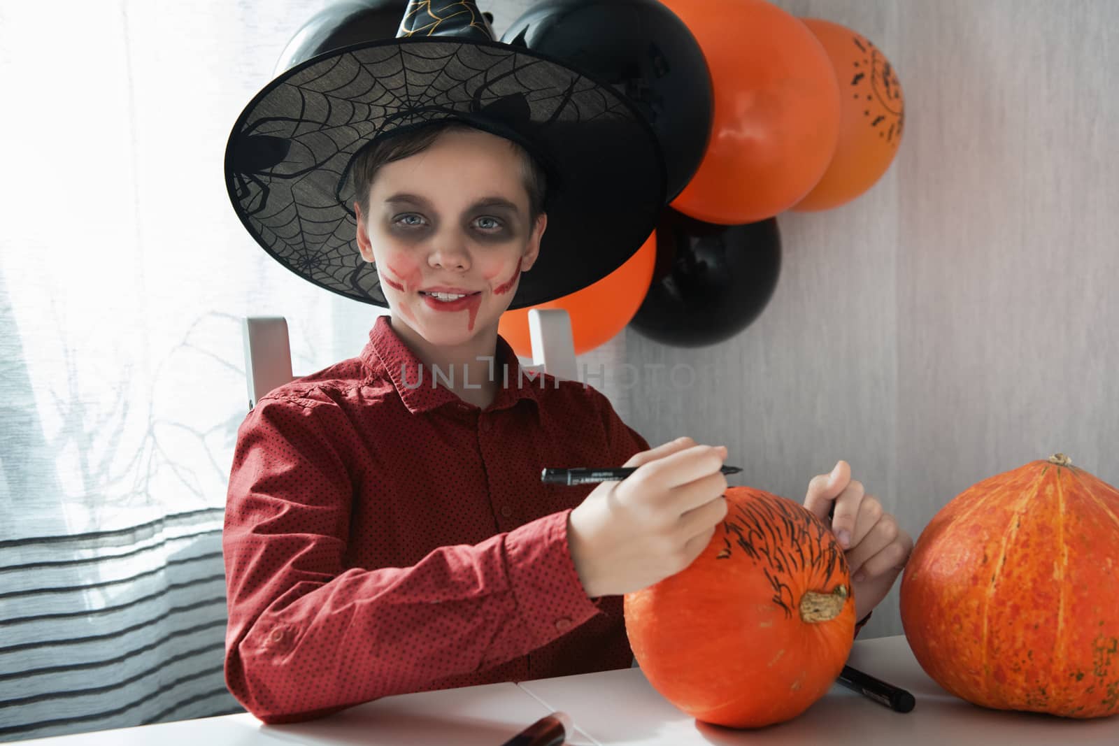Happy teen boy in costume preparing for the Halloween celebration drawing a pumpkin. Halloween carnival or masquerade concept