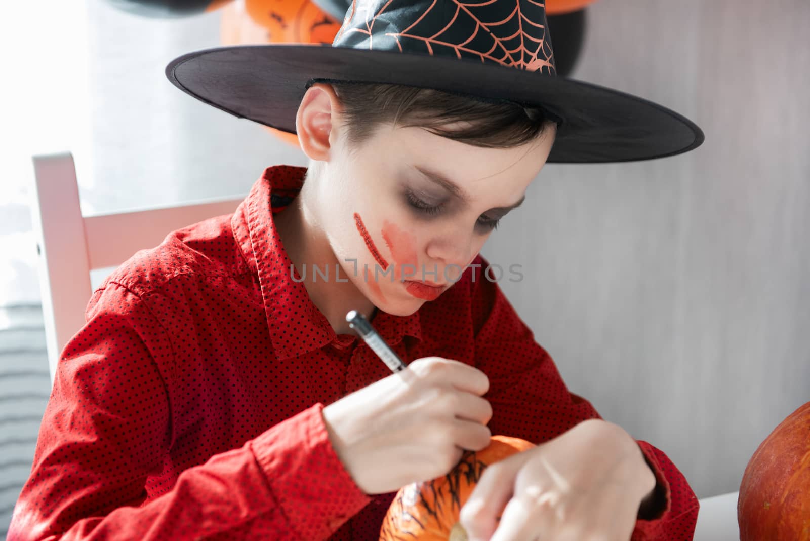 Teen boy in costume preparing for the Halloween celebration drawing a pumpkin. Halloween carnival or masquerade concept