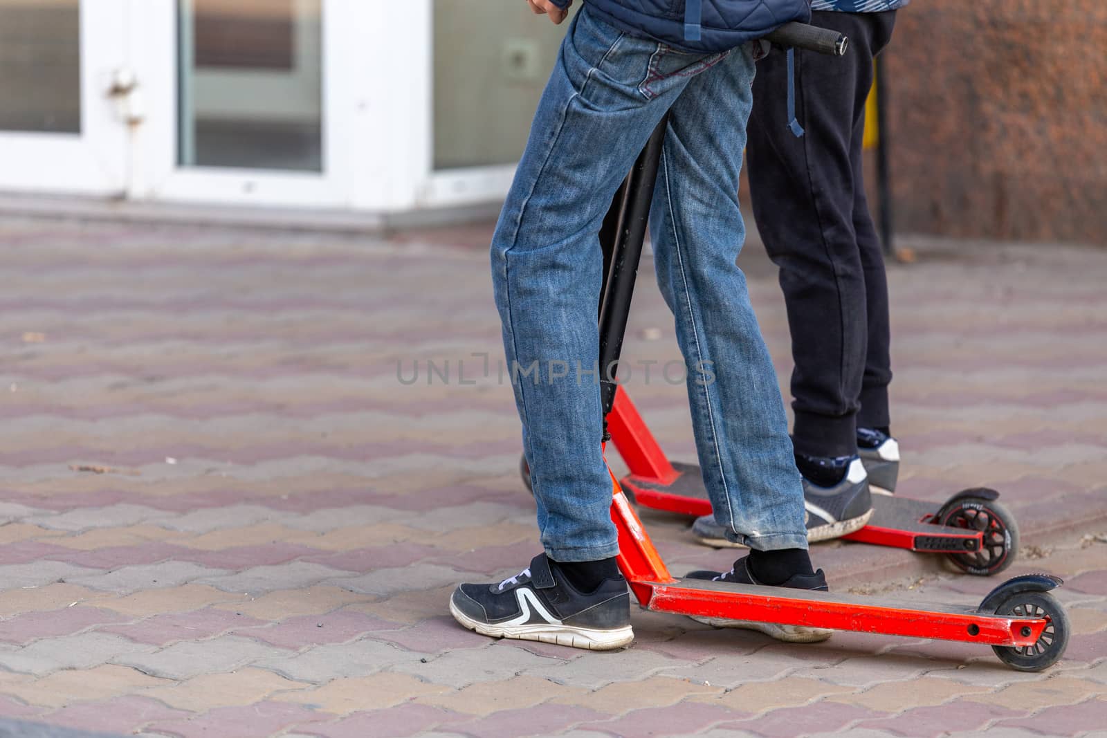 slim kids legs with scooters on the urban pavement sidewalk - closeup witn selective focus.