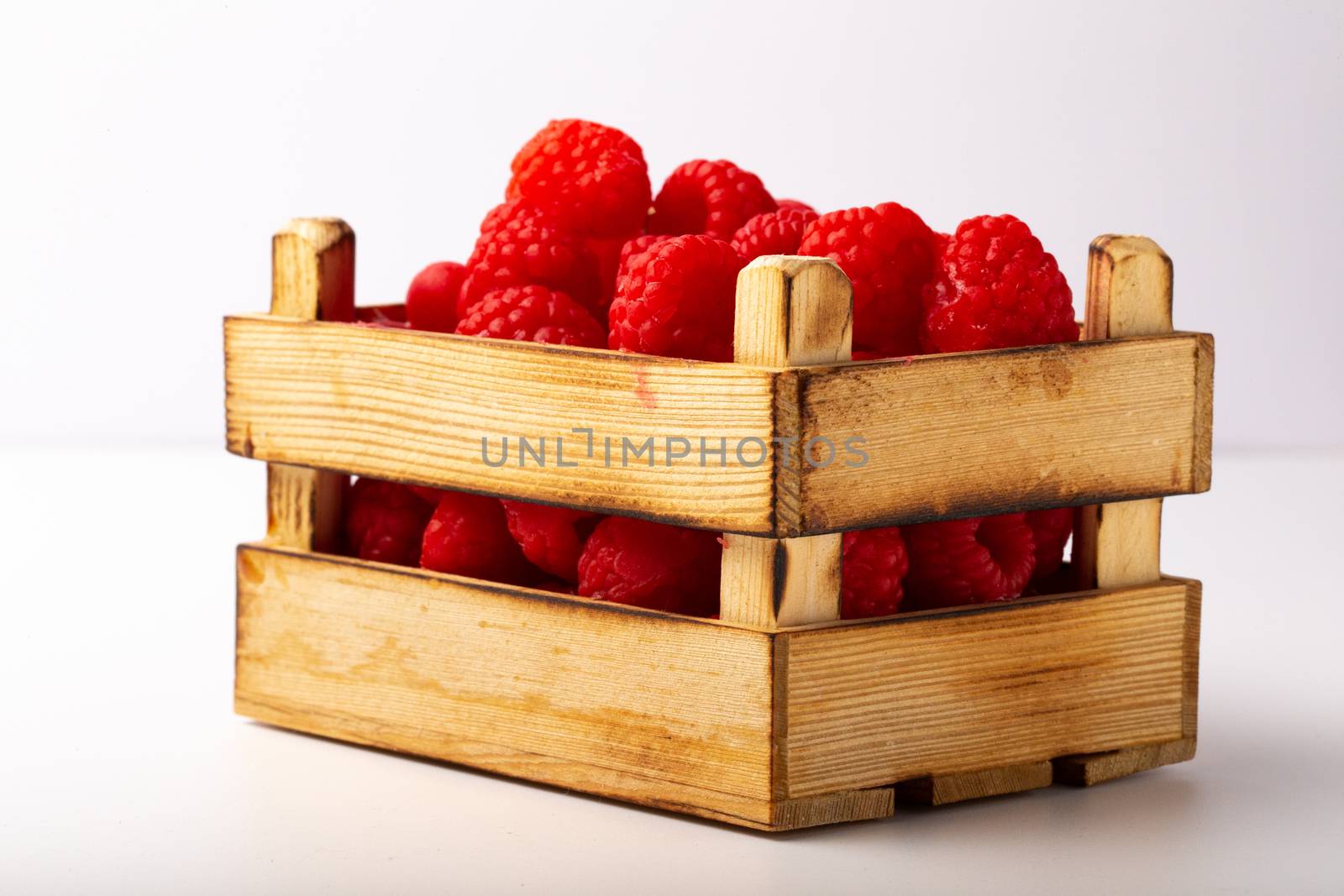 Some raspberries in a small wooden box on a white background