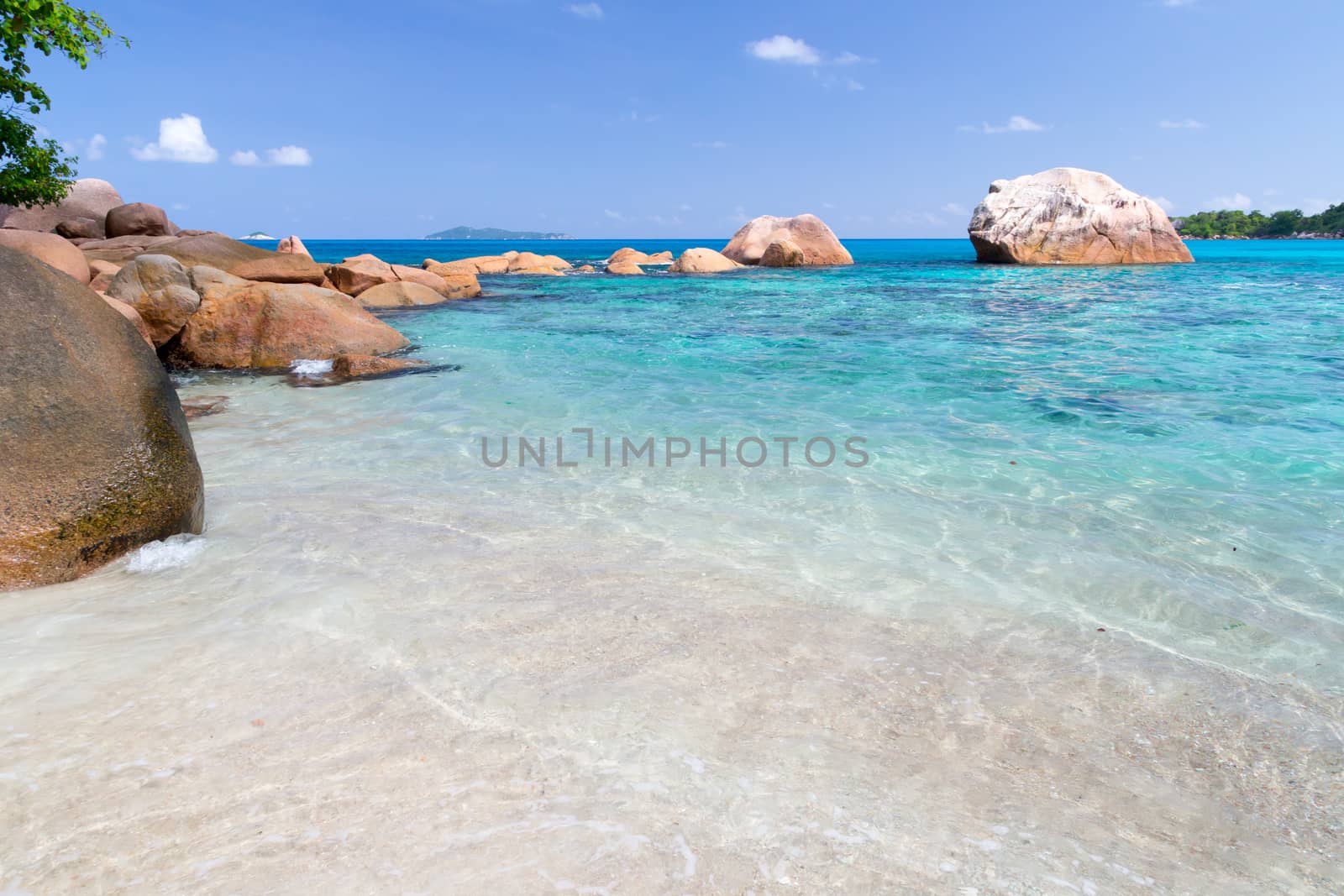 Beach with blue water and blue sky and white sand and some rocks