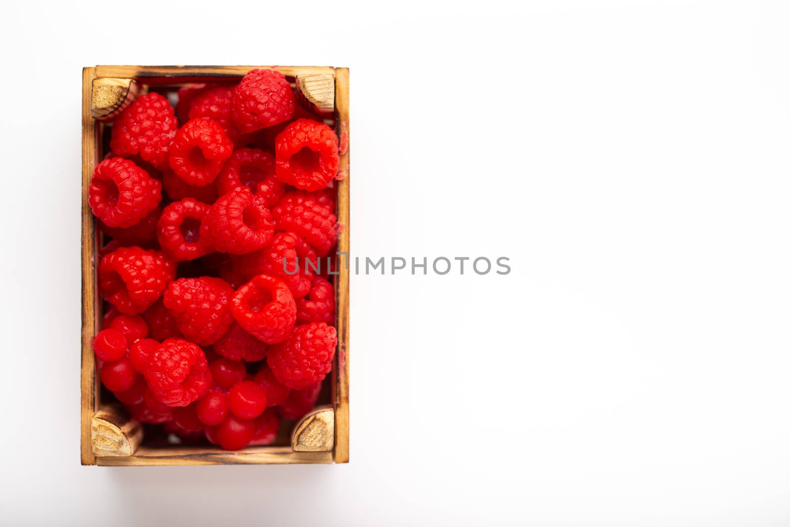Some raspberries in a small wooden box on a white background