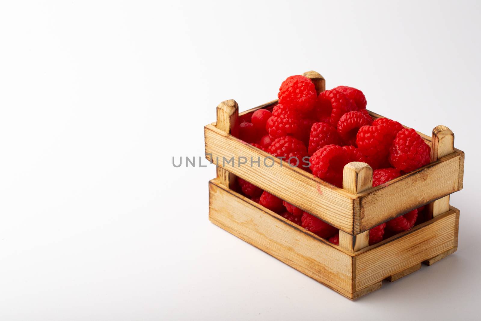 Some raspberries in a small wooden box on a white background