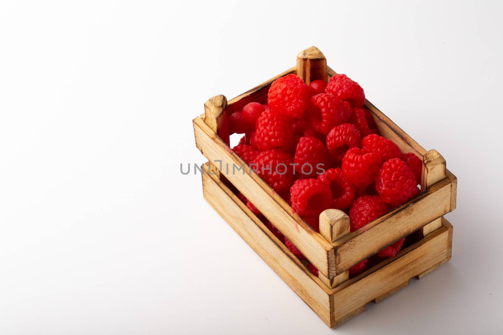 Some raspberries in a small wooden box on a white background