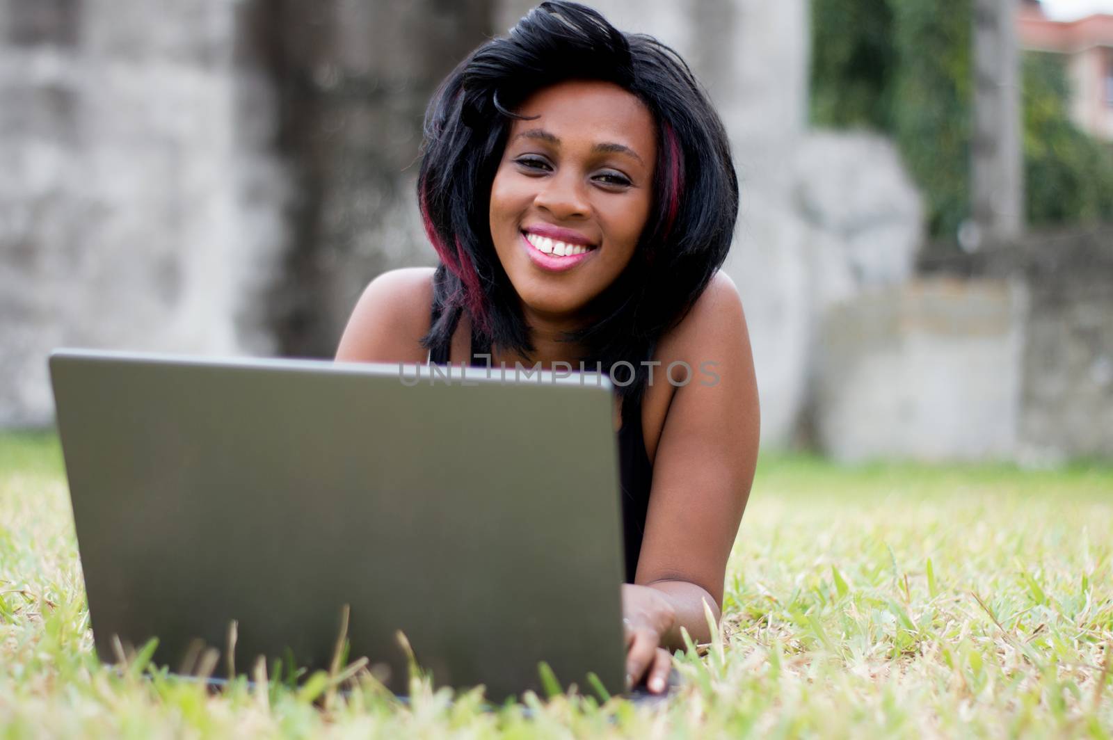 beautiful smiling woman lying on the grass, working on her laptop.