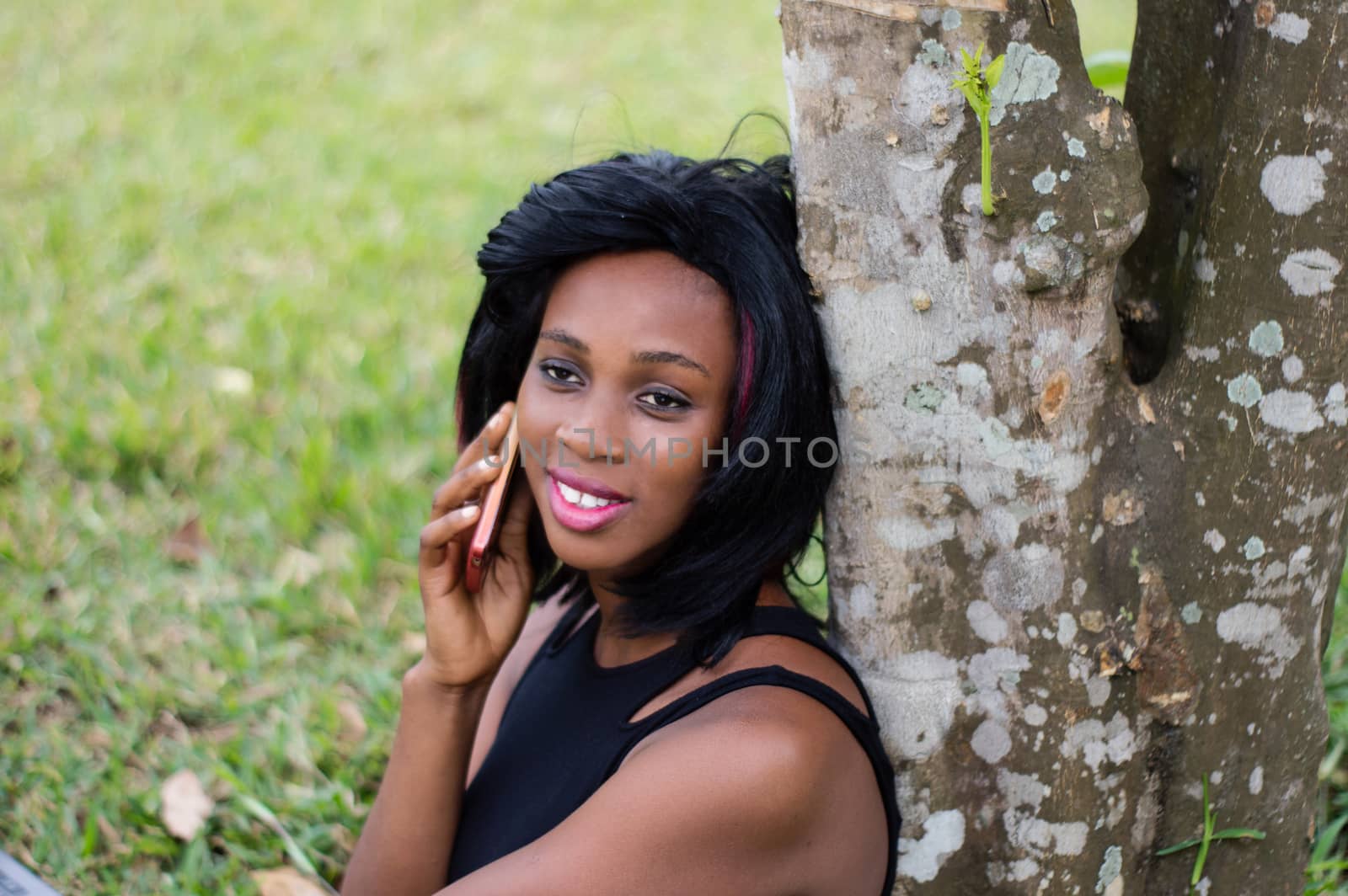 pretty girl sitting next to a tree and talking on the phone in the park