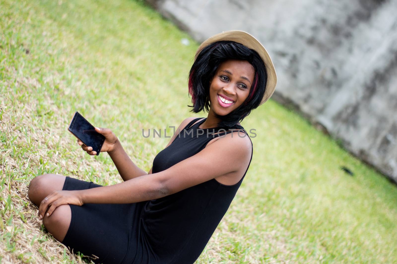 smiling young woman sitting alone in a park and holding a telephone in hand