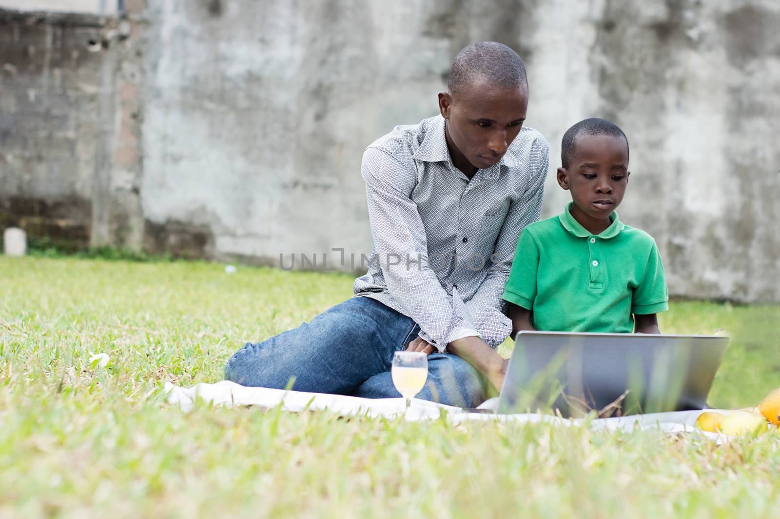 father and son sitting on a white tablecloth working on a computer in the garden