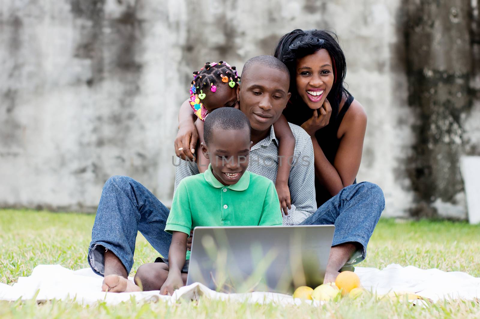 happy family sitting at the park and looking together on a laptop