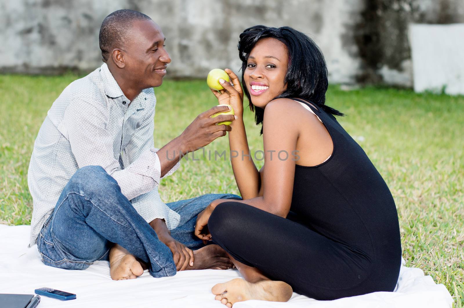 young couple sitting on the grass sharing a green apple together lovingly