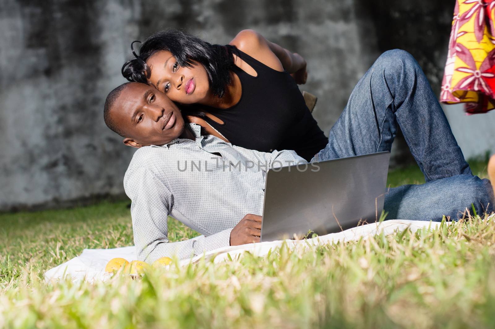 young happy couple lying in love at the park and using a laptop