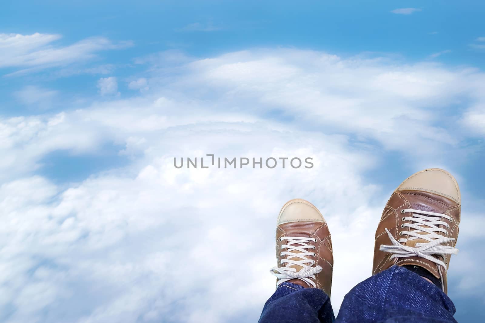 Two legs of the men wore blue jeans statements and brown leather shoes with clouds sky background.