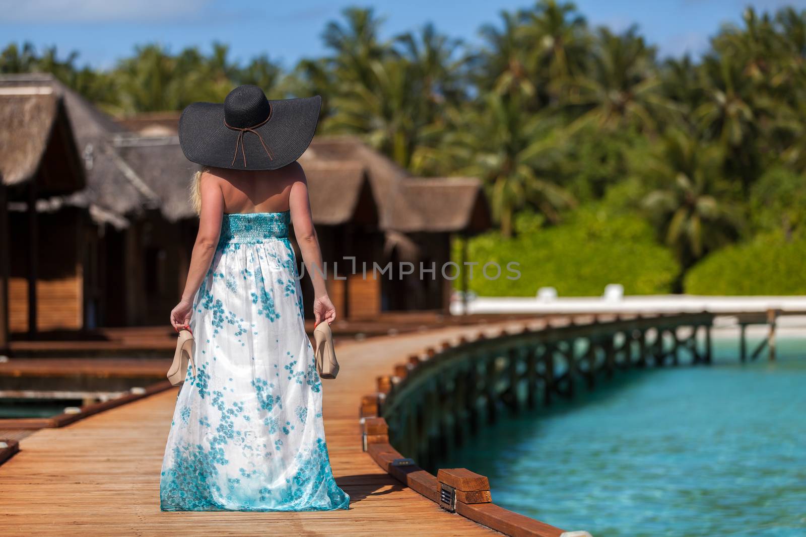 Maldives, young woman walking along the bridge with high heels in the hand and a black hat