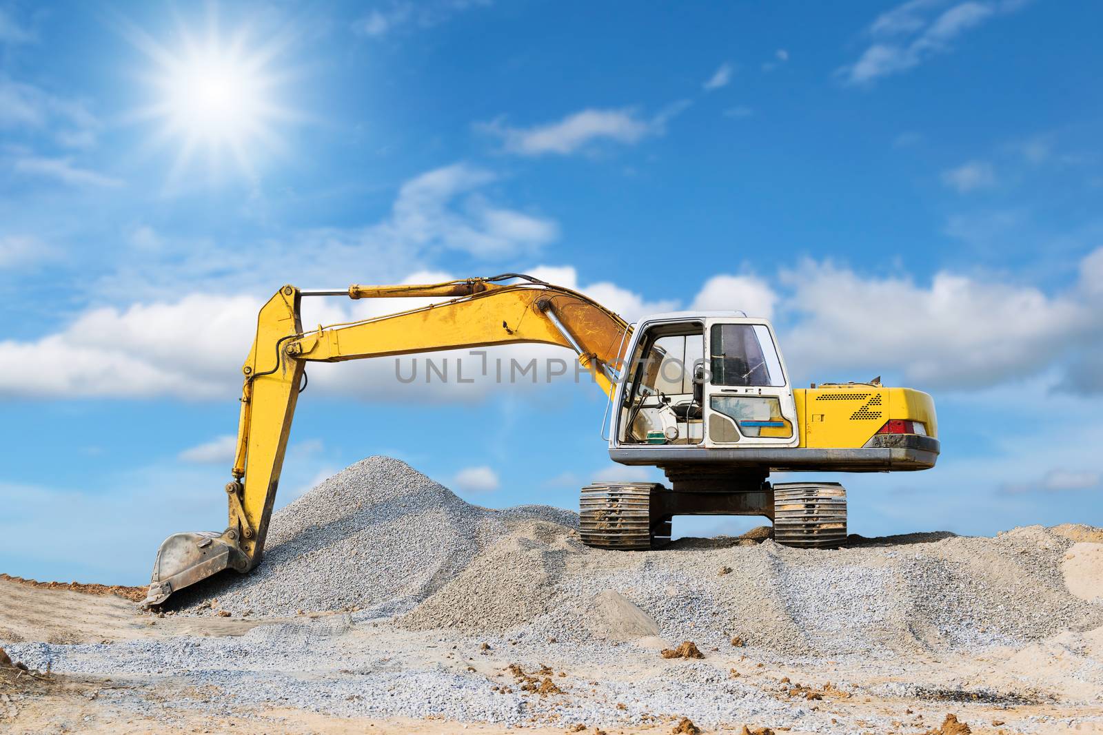 Excavator parked on the mound with sunlight and blue sky background.
