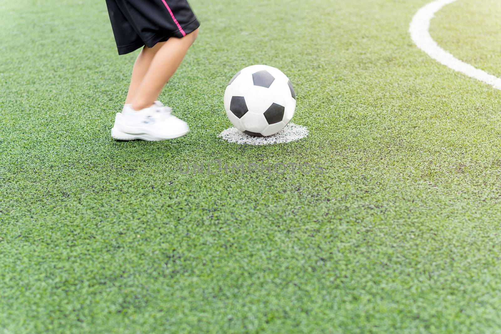 Asian boy playing soccer in the artificial grass field.