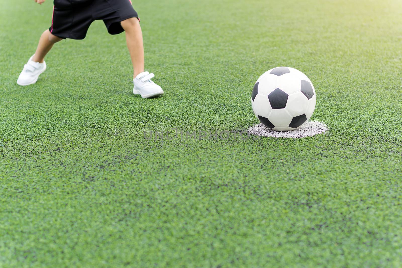 Asian boy playing soccer in the artificial grass field.