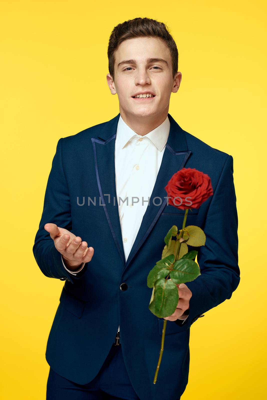 Young man in a classic suit with a red rose in his hand on a yellow background emotions cropped view model. High quality photo