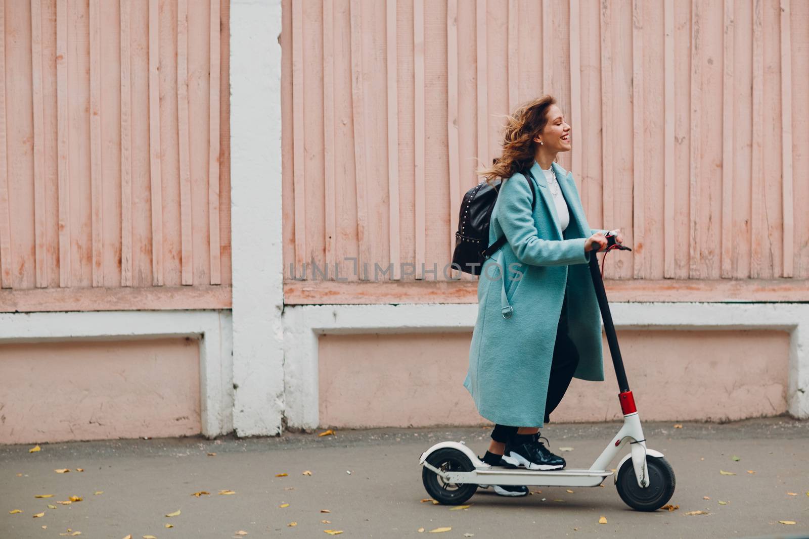 Young woman with electric scooter in blue coat at the city by primipil