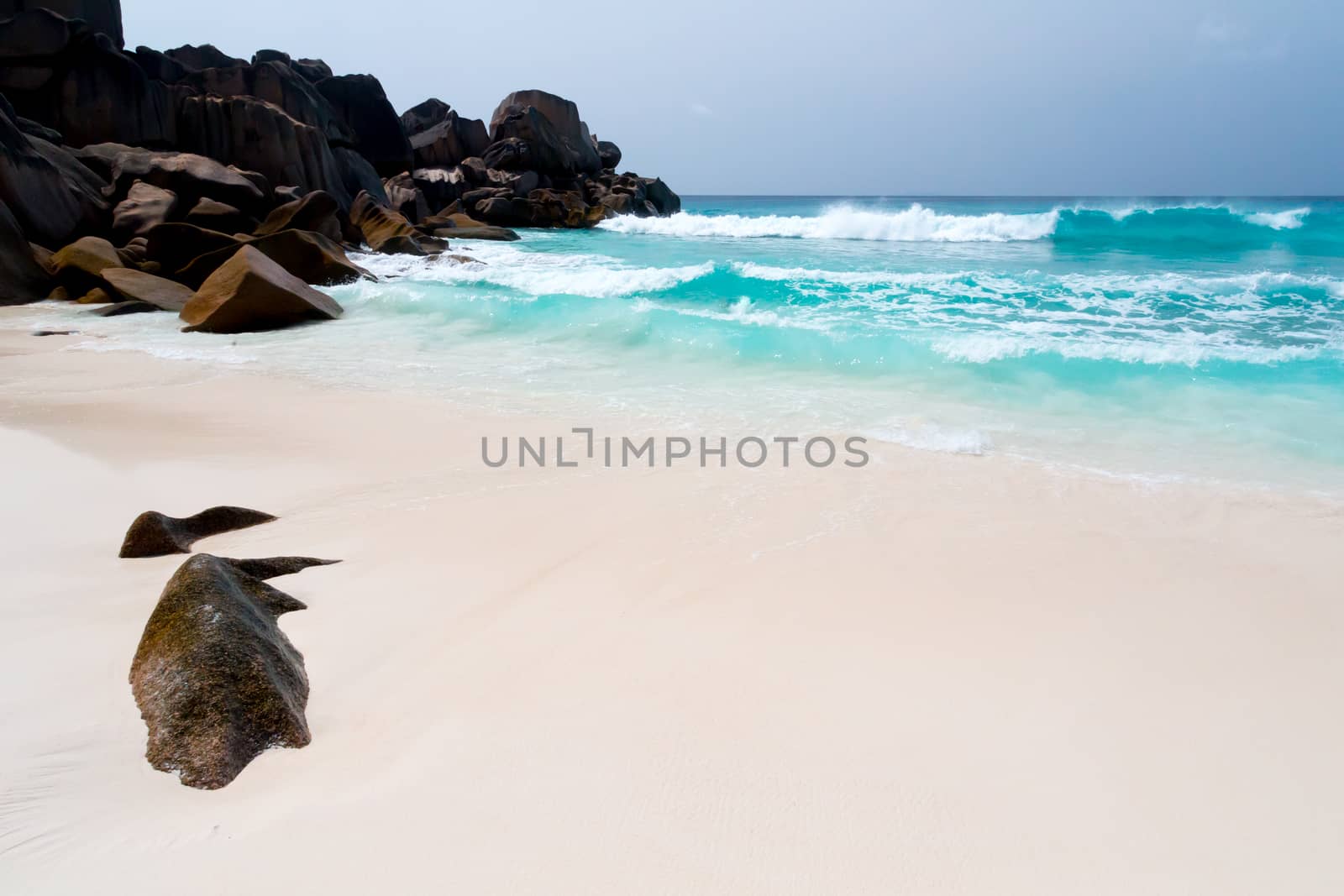 Blue sky and a white sand beach with a lot of big rocks