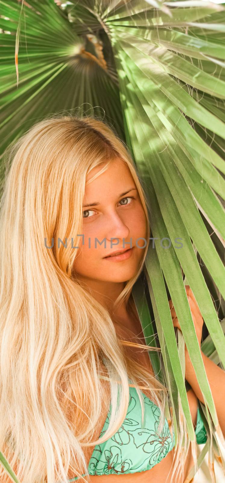 Woman with blond hair wearing bikini, posing near palm tree, beach lifestyle in summertime, holiday travel and leisure concept