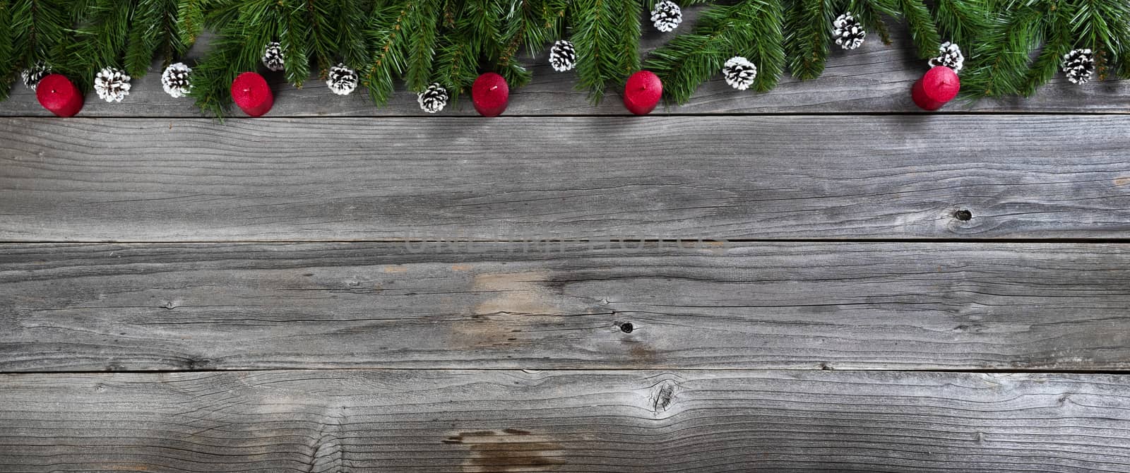 Merry Christmas and Happy New Year concept with red candles inside of fir branches on rustic wooden boards 