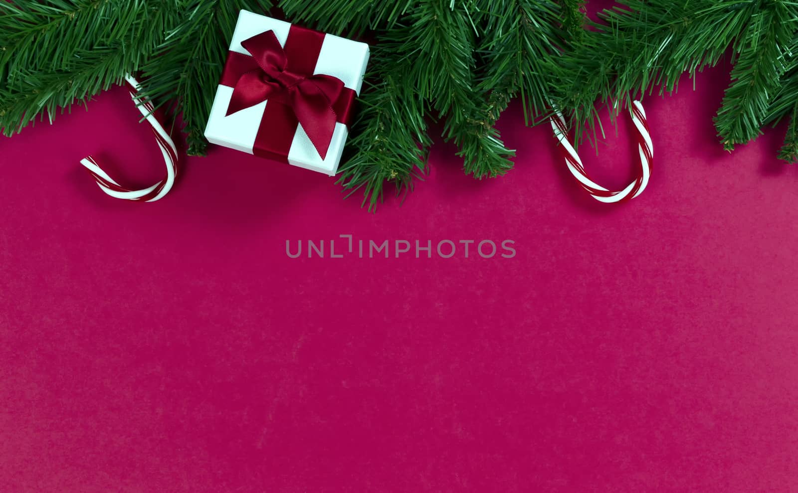 Merry Christmas and happy New Year on a red background with evergreen branches plus candy canes and gift box 